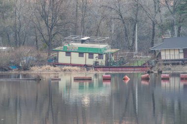 Huzurlu bir rıhtım manzarası, rıhtımda küçük bir tekne, ve ağaçların arasına yerleştirilmiş rahat bir göl evi huzurlu seyahat merkezlerini desteklemek için uygun, tatil önerisi Kyiv, Ukrayna, 09-15-2024