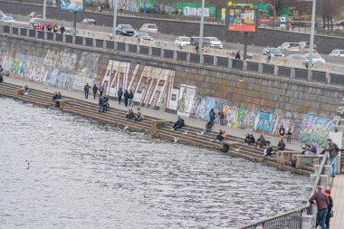 Grafiti kaplı bir duvar, halka açık banklar, tekneler, arabalar ve insanlarla dolu bir şehir sahnesi. Bölge, Kyiv, Ukrayna, 09-15-2024 'ü arayan reklamcılara cazip gelen canlı bir kültüre sahip.