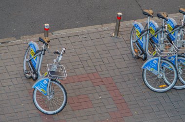 Sepetlerle donatılmış ve zincirlerle güvenlikli bisiklet sıraları şehir kaldırımına park edilmiş durumda. Muhtemelen Ukrayna 'nın başkenti Kyiv' deki bir bisiklet paylaşım programından. 09-15-2024