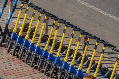 Görüntü, kaldırım ayarı üzerinde sarı ve mavi renkli elektrikli scooter çizgilerini gösteriyor, muhtemelen kiralık veya paylaşımlı bir hareketlilik servisinin parçası. Kyiv, Ukrayna, 09-15-2024 kentsel ulaşımı üzerinde duruluyor.