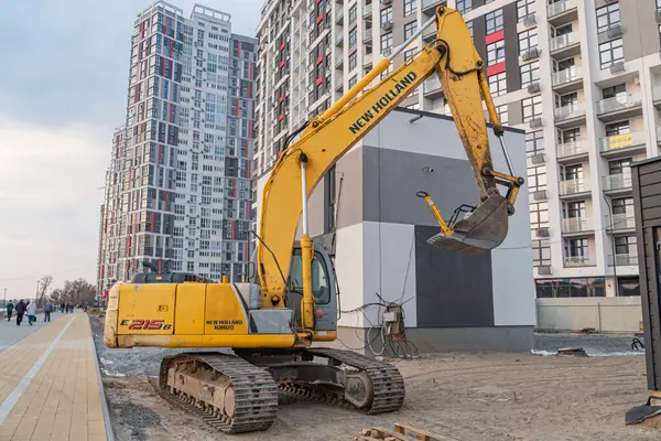 Ukrayna, Kyiv, Ukrayna, 09-15-2024 bulutlu gökyüzü altındaki çok katlı binaların arkaplanına karşı çalışan bir inşaat kazıcısı.