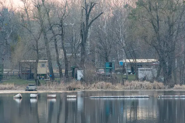 Suyun kenarındaki sakin karavan parkı, rıhtıma yanaşmış teknelerle sakin sular, ağaçları ve binaları yansıtan sakin sular, şafak veya alacakaranlık silueti, dinlenmek isteyen ziyaretçilere hitap eden Kyiv, Ukrayna, 09-15-2024