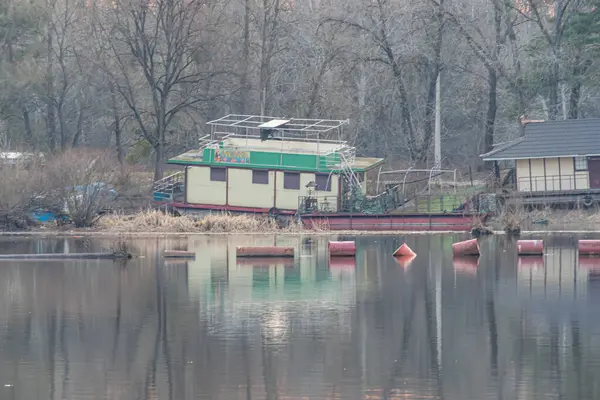 Huzurlu bir rıhtım manzarası, rıhtımda küçük bir tekne, ve ağaçların arasına yerleştirilmiş rahat bir göl evi huzurlu seyahat merkezlerini desteklemek için uygun, tatil önerisi Kyiv, Ukrayna, 09-15-2024