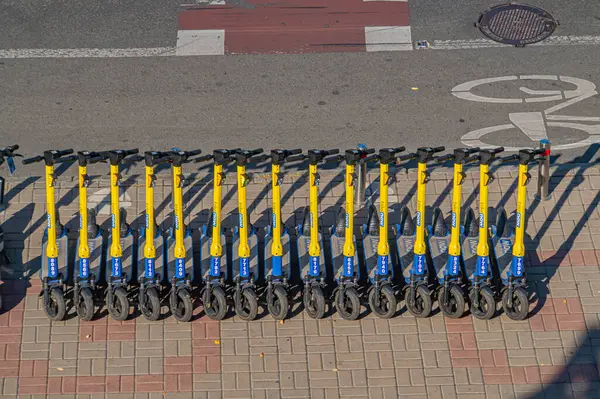 Görüntü, şehir ortamında kaldırımda bir sıra mavi elektrikli scooter gösteriyor, muhtemelen çevre dostu şehir ulaşımını desteklemek için kullanılan bir kiralama şirketinden, Kyiv, Ukrayna, 09-15-2024