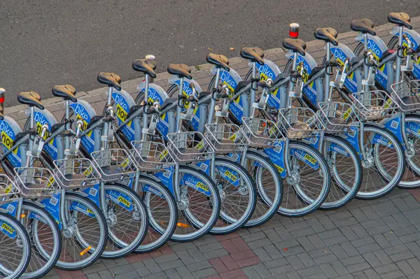 Görüntü, kentsel bir alanda kaldırım kenarına dizilmiş bisiklet paylaşım sisteminin bir parçası olan mavi bisikletlerin düzenli bir sırasını gösteriyor. Görüntü temizlik, modernlik ve uygun Kyiv, Ukrayna, 09-15-2024