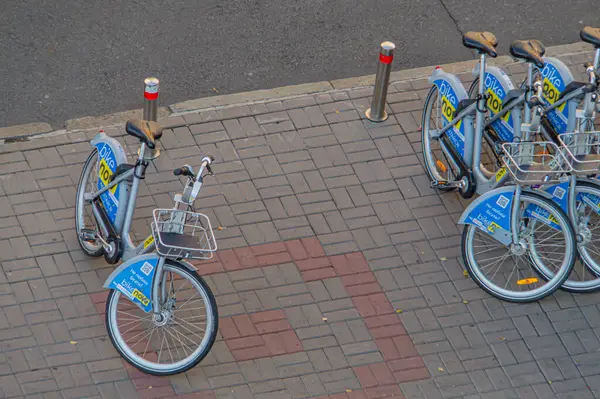 Sepetlerle donatılmış ve zincirlerle güvenlikli bisiklet sıraları şehir kaldırımına park edilmiş durumda. Muhtemelen Ukrayna 'nın başkenti Kyiv' deki bir bisiklet paylaşım programından. 09-15-2024