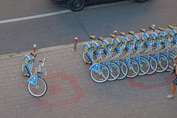 Tuğla kaldırımlara doğru düzgün park edilmiş mavi ve kırmızı bisikletli canlı bir şehir manzarası, bisiklet paylaşım hizmetine veya kentsel bisiklet kültürüne işaret ediyor. Görüntü Orga Kyiv, Ukrayna, 09-15-2024