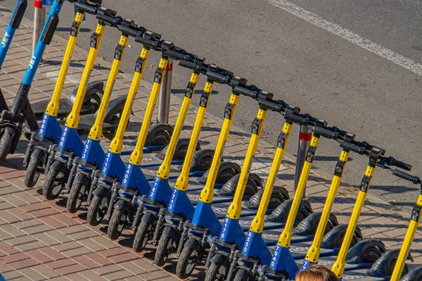 Görüntü, kaldırım ayarı üzerinde sarı ve mavi renkli elektrikli scooter çizgilerini gösteriyor, muhtemelen kiralık veya paylaşımlı bir hareketlilik servisinin parçası. Kyiv, Ukrayna, 09-15-2024 kentsel ulaşımı üzerinde duruluyor.