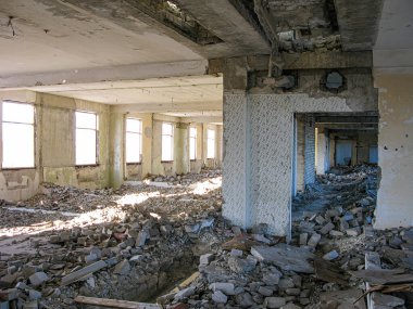 Görüntü, enkaz, kırık malzemeler ve maruz bırakılan yapısal elementlerle hasar görmüş bir iç mekan tasvir ediyor. Pencereler toz ve kirle kaplı, dışarıya bakmıyor. Tarz, gizli fotoğrafı gösteriyor.