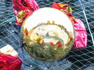 Kırmızı metalik cisimlerle çevrili kış sahnesini yansıtan ışıklandırılmış Noel ampulünün yakın çekimi