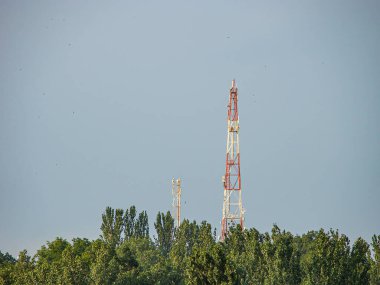 Görüntü gösteriyor ki, telekomünikasyon kuleleri uzun, kırsal alanda çoklu anten, ağaçlar ve yeşillik kısmen bereketli yeşil bitki örtüsü daha sıcak bir mevsim görüntüsü veriyor.