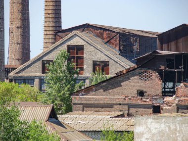 Terk edilmiş, çürüyen bir endüstriyel kompleksin panoramik görüntüsü açık pencere ve çatı hasarı açık gökyüzü, arka plandaki uzun bacalar eski üretim alanlarını işaret ediyor