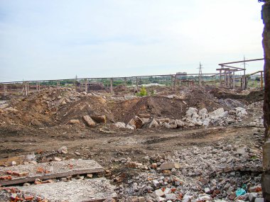 Görüntü yıkımın ıssız bir sahnesini tasvir ediyor, molozlarla, düzleştirilmiş yapılarla, ve bulutlu gökyüzüne karşı güç hatlarıyla hayatta kalan bitki örtüsü kalıntıları arasında.