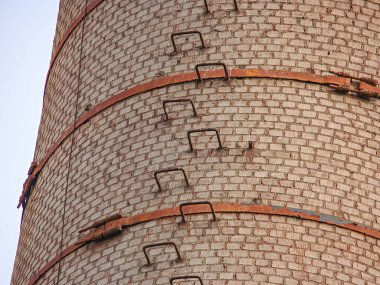 Eski, kırmızı tuğlalı bir bacaya ya da paslı metal bileşenlerine sahip bir kuleye yakın plan bulutlu bir gökyüzünü işaret ediyor.