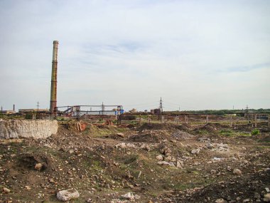 Resim, enkaz ve hasarlı yapılarla parçalanan ya da temizlenen endüstriyel bir manzara resmediyor. Arka planda bir vinç görünüyor. Gökyüzü bulutlu.