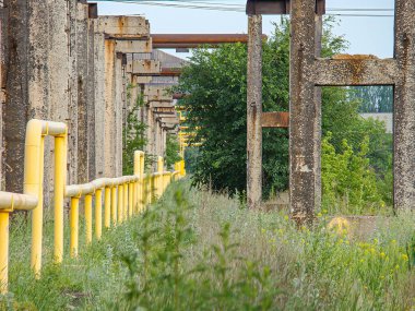 Sarı boyanmış metal boruların görüntüsü, muhtemelen endüstriyel bir yapı ya da kompleksin bir parçası borular beton sütunlar tarafından destekleniyor ve üstlerinde aşırı büyük bir taşıma sistemi var.