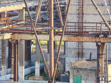 Görüntü terk edilmiş bir sanayi bölgesini gösteriyor, muhtemelen sökülmüş bir tersane ya da fabrika Rusty metal yapıları, enkazla düz olmayan zemin, zıt yeşil çimen tarlası, ve gizli dokümantasyon tarzı
