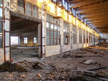 Açıkta duran tuğla duvarları, yerdeki döküntüler, ahşap kirişler, doğal ışıklandırma ve çürüyen çöküntülerle terk edilmiş bir sanayi bölgesi.