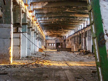 Yüksek tavanlar, açıkta kalan borular, geniş pencerelerden sızan doğal ışık, enkaz kaplı zemin, kapalı bir kapıya çıkan merdiven, yıpranmış ve çürüyen duvarlar, ihmal ve terk edilmişlik.