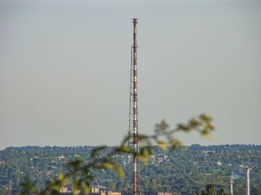 Görüntü, bulutlu bir gökyüzünün altında çoklu antenleri olan uzun ve ince bir iletişim kulesi gösteriyor.