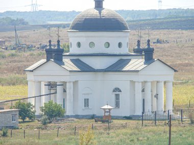 Doğu Ortodoks mimarisinin tipik özelliklerine sahip birden fazla kubbesi olan beyaz bir kilise açık kırsal ya da yarı kırsal alanda gösteriliyor.