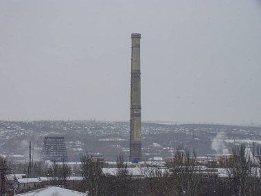 Karlı bir günde diğer yapıların arasında uzun bir bacanın yer aldığı kentsel bir sanayi sahnesi.