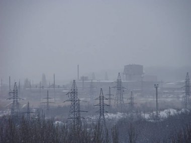 Bir endüstriyel kompleksin uydu görüntüsü, muhtemelen bir elektrik santrali ya da benzeri bir tesis, karla kaplı yapılar ve duman bulutları yayan bacalar.
