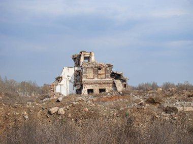 Açık hava sahnesi gündüz saatlerinde kısmen çökmüş, yıkılmış, enkaz altında kalmış, insan aktivitesi olmayan bir bina gösteriyor.