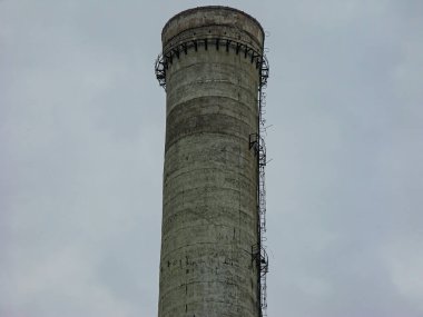 Bulutlu bir gökyüzüne karşı yıpranmış, çok bantlı bir baca. Yapının tepesinde dış bir yürüyüş yolu bulunur ve elementlerden aşınma izleri gösterir.