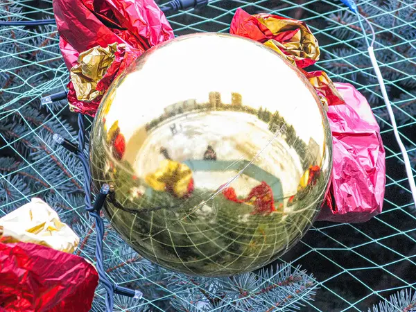 Kırmızı metalik cisimlerle çevrili kış sahnesini yansıtan ışıklandırılmış Noel ampulünün yakın çekimi