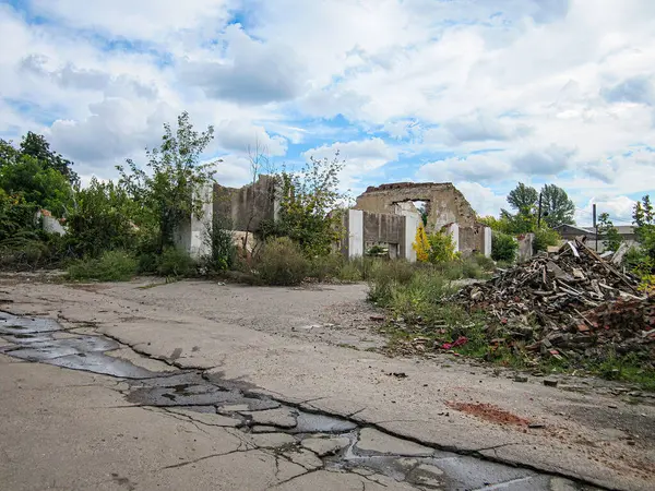 Kırık yol ve çürüyen bina ile kentsel bozulma sahnesi, açık mavi gökyüzü enkazı ile zıt, bir zamanlar hareketli bir çevreye işaret ediyor, şimdi terk edilmiş.