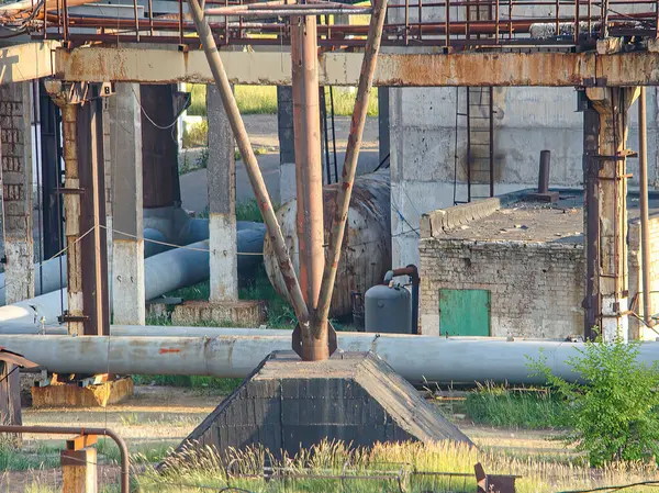 Beton bir platformun üzerinde geniş bir vinç bulunan aşırı gelişmiş bir sanayi sahnesi, aşınma izleri gösteriyor. Diğer özellikler arasında havalandırma boşlukları, kanallar ve otlar ve küçük otobüsler gibi bitkiler yer alıyor.