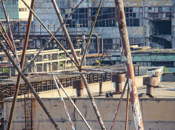 Terk edilmiş bir sanayi yapısının görüntüsü, muhtemelen bir fabrika ya da depo. Bina, kırık camlar, hasarlı çatılar, yıpranmış duvarlar ve iskele ile harap olmuş.-