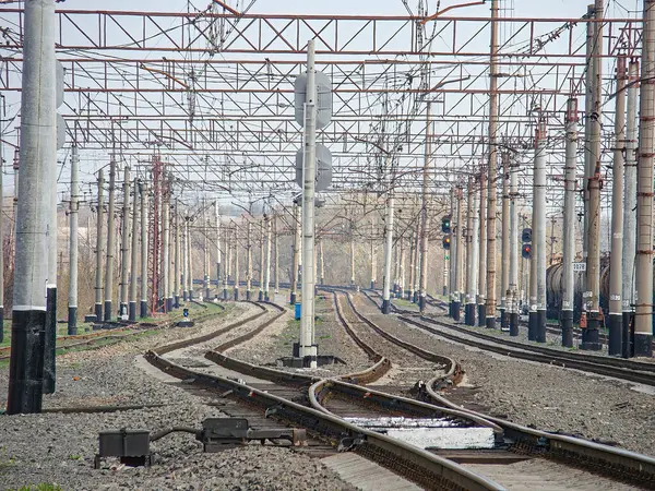 Çoklu rayları olan elektrikli bir demiryolu kavşağı, yukarıdaki elektrik hatları, bulutlu gökyüzü, tren yok, sinyal girişleri, üst katenizasyon sistemleri, raylı balast, t içinde olası işletim binası