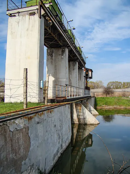 Görüntü, su altında beton bir yapıya, muhtemelen bir baraj veya sel bariyerine sahip bir sanayi sahnesini tasvir ediyor, aşınma izleri su seviyesine çıkan merdiven kısmen de olsa