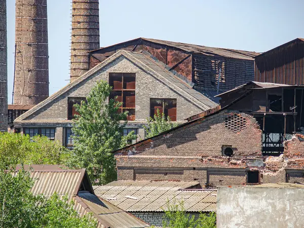 Terk edilmiş, çürüyen bir endüstriyel kompleksin panoramik görüntüsü açık pencere ve çatı hasarı açık gökyüzü, arka plandaki uzun bacalar eski üretim alanlarını işaret ediyor