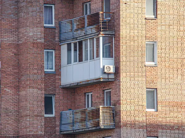 Görüntü, çok katlı, balkonlu ve pencereli kırmızı tuğlalı bir bina gösteriyor.