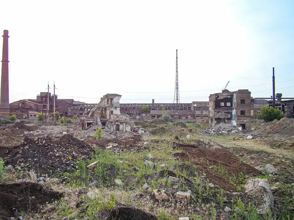 Endüstriyel dönüşüm sonrası terk edilmiş bir sanayi manzarası ya da çevresel restorasyon enkazı, bitkiler ve molozlar, harabelerin arasında duran uzun bir baca ile bölgeye hükmediyor.