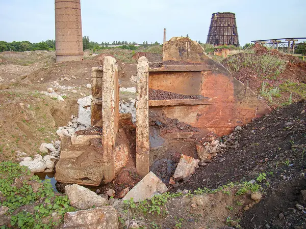 Paslı metal bir çerçeve, beton sütunlar ve arka planda çürüyen yapılarla betimlenmiş terk edilmiş bir sanayi ya da inşaat alanı.