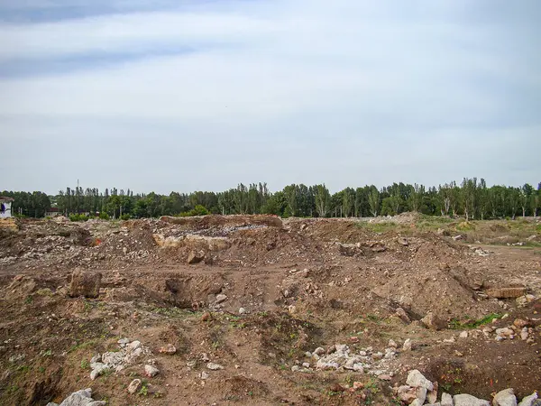 Kazı, düzensiz zemin, toprak ve enkaz yığınları, inşaat veya peyzaj işleri, toprak ve kaya yığınları, bulutlu gökyüzü, ağaçlar çizgisi, çimenler