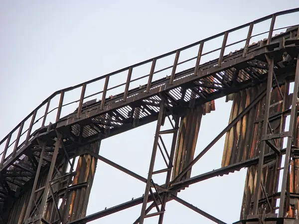 Hız trenleri ya da iskeleye benzer koyu metalik yapılara sahip soyut desenli kompozit bir görüntü. Elementler eğlence dünyasının tipik bir tasarımı olan tekrarlanan eğri bir dizaynla düzenlenmiştir.