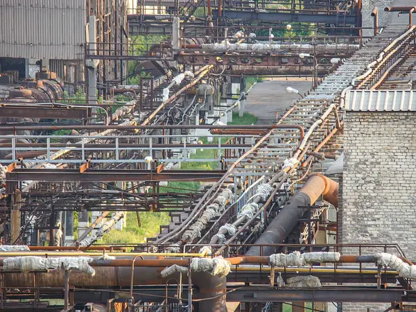 Görüntü, birbirine bağlı birden fazla boru ve tuğla bacası bulunan endüstriyel bir kimyasal ya da petrol işleme tesisini gösteriyor. Tesis muhtemelen doğaya yakın bir yerde, kontrol altında tutuluyor.