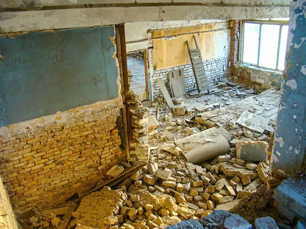 Görüntü, yıkıntılarla, yıkılan parçalarla ve açıkta kalan tuğlalarla dolu terk edilmiş ya da güvensiz bir binanın hasarlı iç kısımlarını gösteriyor. Tavanda görünür çatlaklar var.