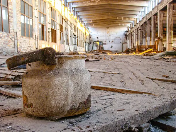 Çürüyen ahşap zemin ve eğri büğrü metal duvarları olan terk edilmiş bir sanayi bölgesi. Dağılmış metal duvarlar. Doğal ışık, ıssızlığı işaret ediyor.