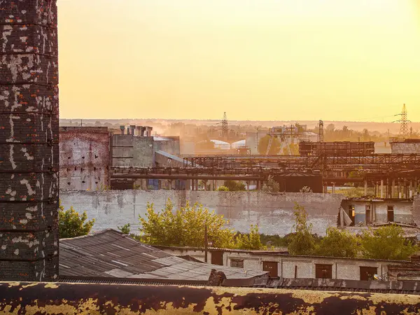 Görüntü, muhtemelen gün doğumunda ya da batımında eski endüstriyel yapıları, terk edilmiş depoları ve zıt modern gökdelenleri gösteren bir şehir manzarası tasvir ediyor.