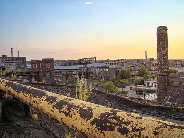 Görüntü, gün batımında, sıcak renklerle soğuk ve yıpranmış binalar arasındaki zıtlık ve çürüyen yapılarla birlikte kentsel bir sanayi sahnesini betimliyor.