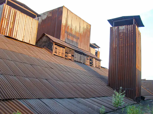 Çürük metal veya ahşap duvarları ve yamalı çatısı olan eski bir bina. Binanın sağ tarafında baca yığınları var. Bu da kapalı bir ateş kaynağı olduğunu gösteriyor.