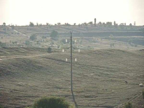 Yuvarlanan tepeler, kurak arazi, elektrik direkleri, kırsal yapı, bulutlu gökyüzü, muhtemelen çöl bölgesi.