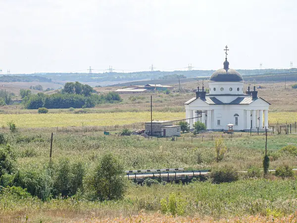 Geleneksel bir binası, yemyeşil bahçesi ve berrak bir gökyüzünün altında açık arazisi olan kırsal bir arazi. Binanın beyaz bir cephesi, dekoratif unsurları, panjurlu pencereleri ve bir kubbeyi işaret eden bir kubbesi var.