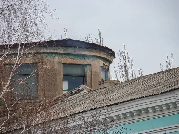 Eski, yıpranmış pencereli bir bina, yanmış bir üst ve dağınık molozla kentsel çürüme içinde duruyor. Olay yeri geçmiş hasarları ve ihmalleri gösteriyor.